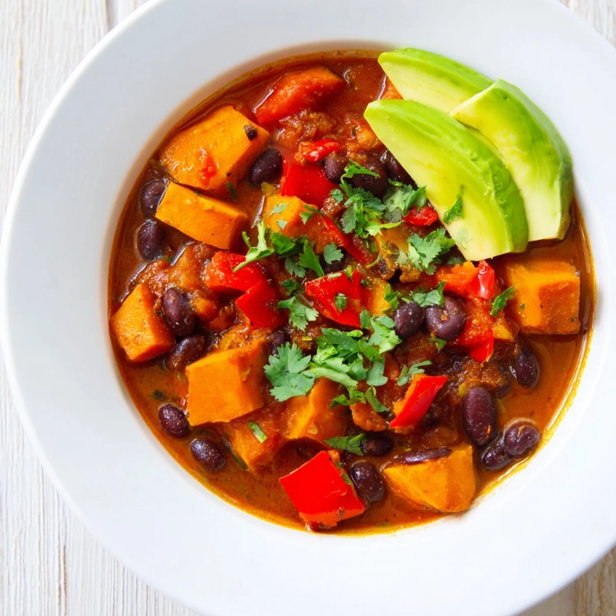 Steaming bowl of Sweet Potato & Black Bean Chili, garnished with fresh cilantro and a lime wedge.