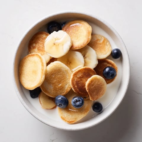 Mini pancake cereal served in a bowl, topped with fresh berries and syrup.  