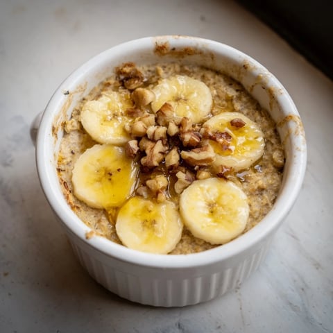 Golden-brown Baked Oats Ramekins with Banana, topped with sliced bananas and a drizzle of honey.