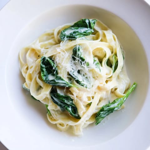 Fresh fettuccine noodles tossed in a rich garlic cream sauce with vibrant spinach, garnished with parsley and extra Parmesan.  