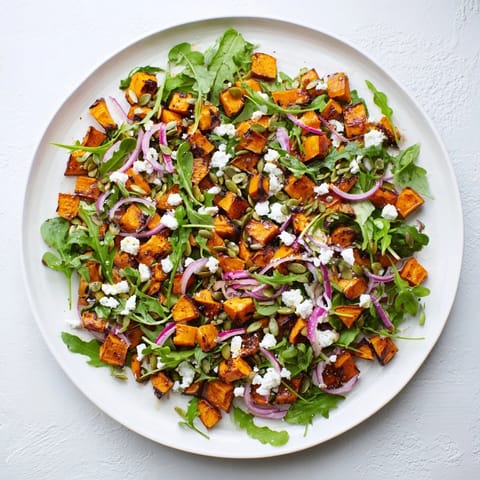 Vibrant roasted sweet potato salad featuring caramelized cubes, crumbled feta, and red onion on a bed of fresh arugula.