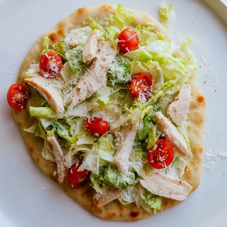 Freshly baked Chicken Caesar Flatbread served on a wooden board, garnished with tangy Caesar dressing and halved cherry tomatoes.